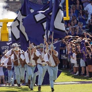 Dressed like cowboys, the TCU Rangers run with large flags at a football game